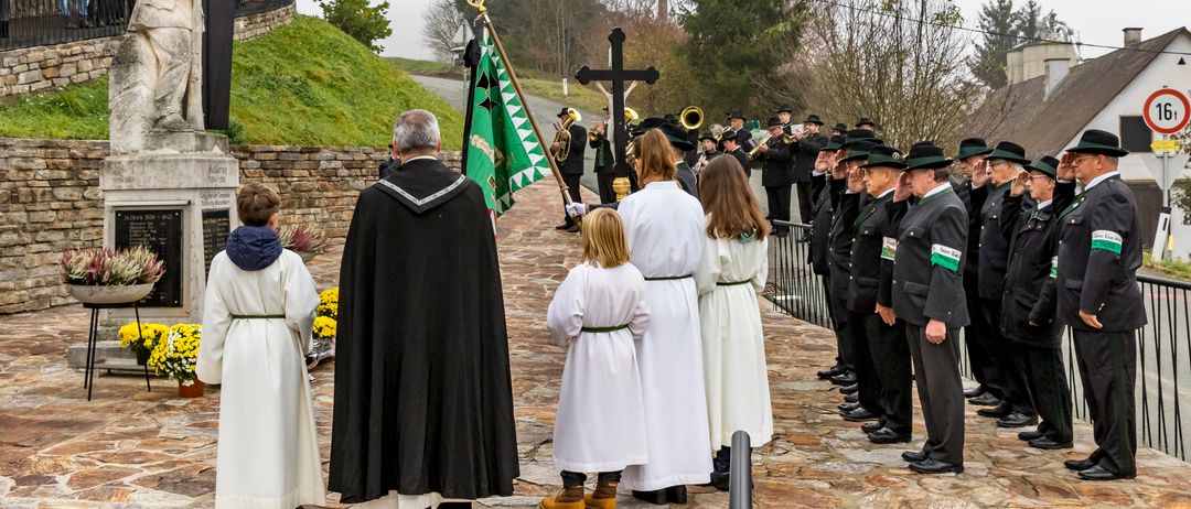 Eine Gruppe von Menschen in zeremonieller Kleidung versammelt sich um ein Kreuz auf einem Hügel mit Zuschauern und einer Band.