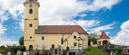 Eine gelbe Kirche mit einem roten Turm und einer Uhr steht prominent in einem Friedhof. Das Gebäude hat ein rotes Dach, und Kreuze und Grabsteine sind im Vordergrund sichtbar.