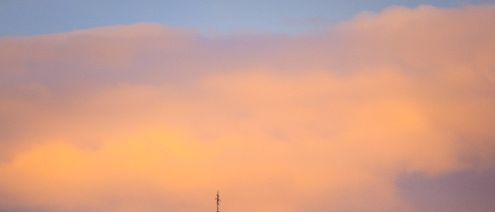 Eine Kirche mit einem hohen Turm steht in einer ländlichen Umgebung unter einem farbenfrohen Sonnenuntergangshimmel, umgeben von Bäumen und Gras.