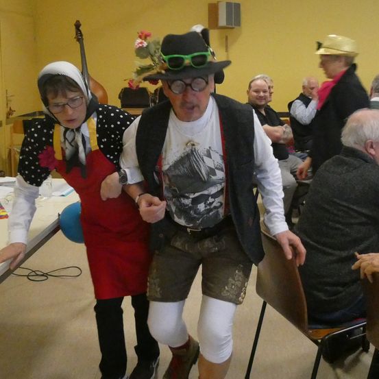 Ein Mann und eine Frau in Kostümen tanzen in einem Raum, in dem andere Leute auf Stühlen sitzen.