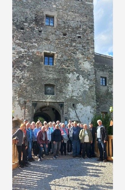 A group of people are standing in front of a large castle. They are all smiling and appear to be taking a group photo.