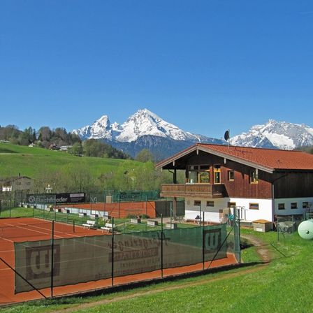 Ein Tennisplatz mit einem roten Dachhaus und einer Bergkette im Hintergrund.