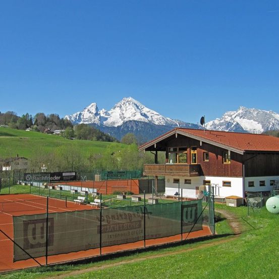 Ein Tennisplatz mit einem roten Dachhaus und einer Bergkette im Hintergrund.