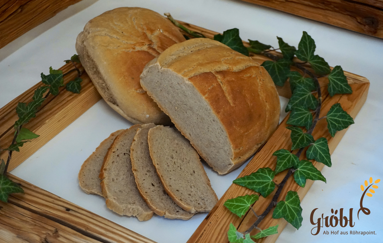 Ein Brotlaib mit einigen Scheiben auf einem weißen Tablett, geschmückt mit grünen Blättern.