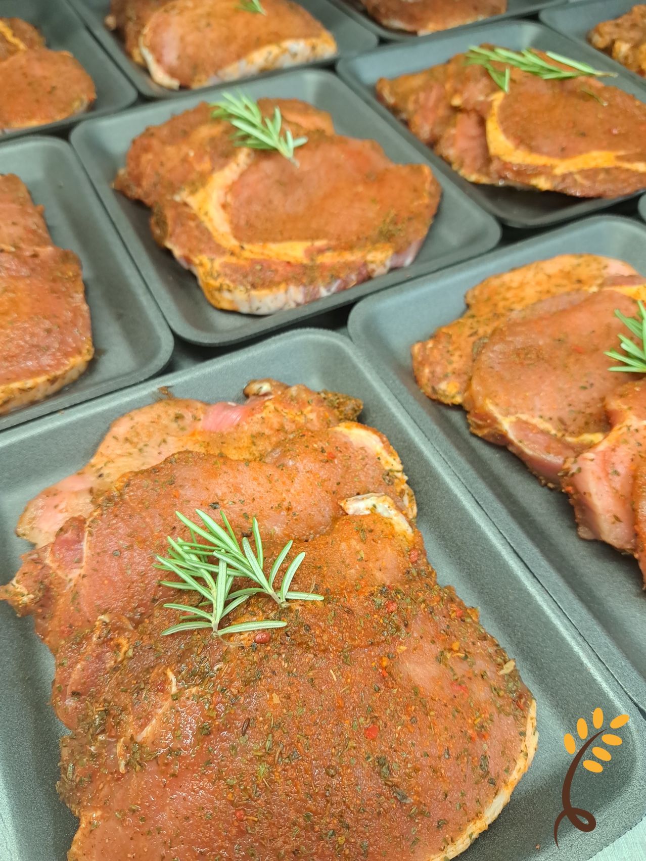 Eine Nahaufnahme von mehreren gewürzten Schweinekoteletts mit Rosmarin auf einem grauen Tablett, bereit zum Kochen.