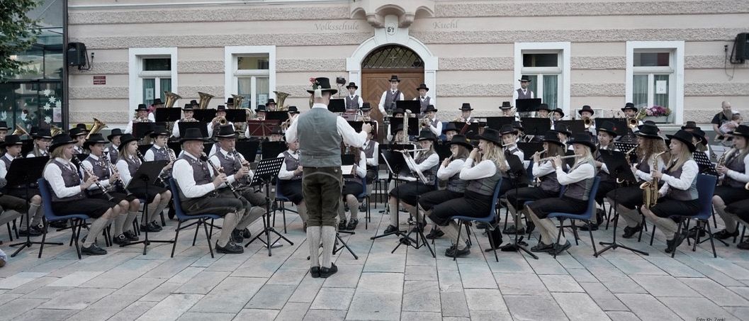 Eine Werbung für ein Musikevent zeigt eine Band, die vor einem Gebäude mit weißen Fenstern auftritt. Die Veranstaltung trägt den Titel 'Marktkonzerte' und enthält Daten und Uhrzeiten.