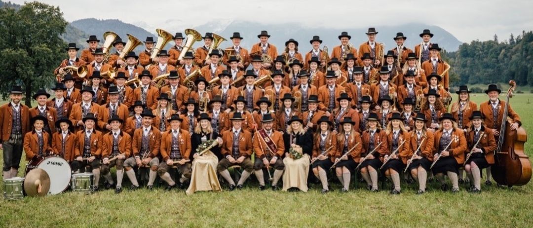 Ein Plakat für ein Musikband-Konzert. Die Band sitzt auf dem Gras. Zeiten sind 19:30 und 11:00 Uhr.