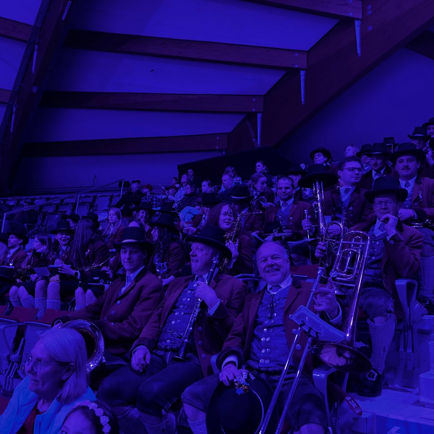 A group of musicians in vintage attire, seated and playing brass instruments in a dimly lit room with a purple ambiance.
