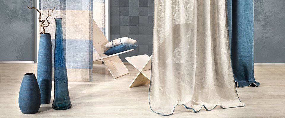 Ein Zimmer mit Holzboden, blau-weiß gestreifter Wand, zwei blauen Vasen, einem Holzstuhl mit Kissen und einem weißen Vorhang mit Muster.