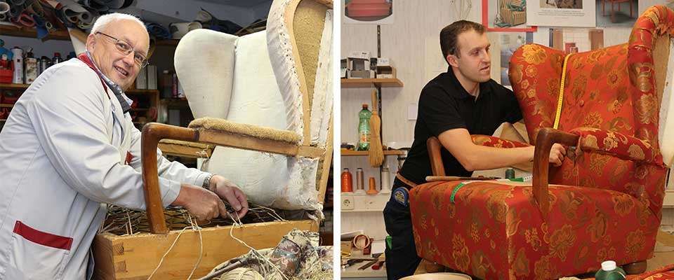Zwei Männer arbeiten an einem Sessel, einer mit weißer Polsterung und der andere mit roter Blumenpolsterung. Beide Männer tragen schwarze Hemden und Hosen.