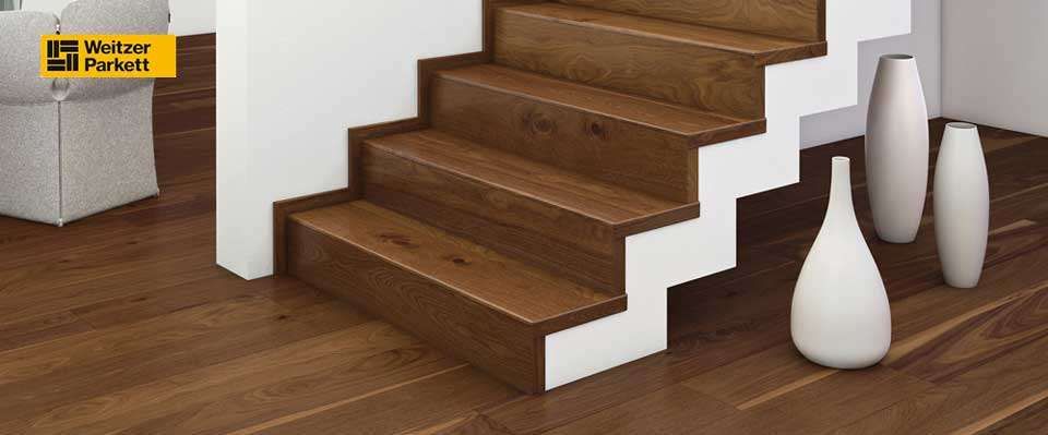 Eine moderne Holztreppe mit weißen Stufen und einem weißen Geländer. Zwei weiße Vasen stehen auf dem Boden.