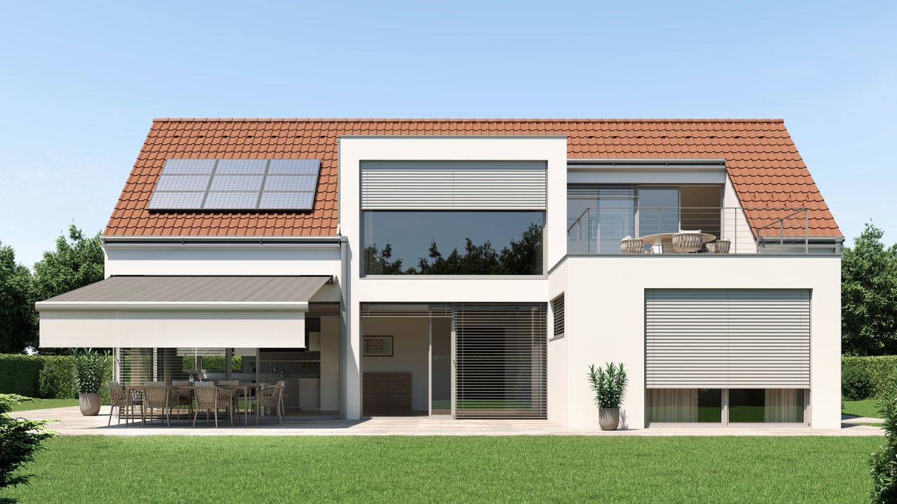 Ein modernes Haus mit einem braunen Dach und Solarmodulen. Die Fenster haben weiße Jalousien. Ein Balkon hat einen Tisch und Stühle. Ein großer grüner Rasen ist vor dem Haus.