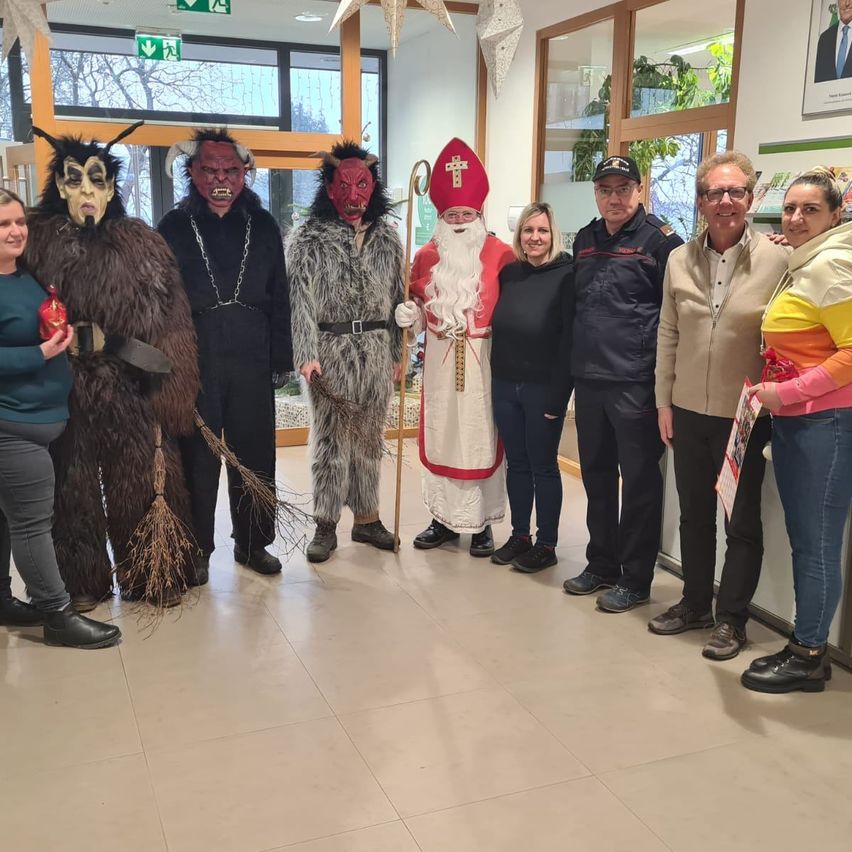 Eine Gruppe Erwachsener in verschiedenen Kostümen, darunter ein Weihnachtsmann, posiert für ein Foto in einem Flur.