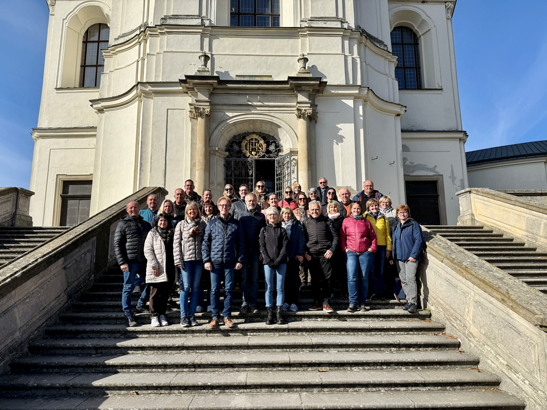 Eine Gruppe von Menschen steht auf den Stufen vor einem historischen Gebäude mit einem goldenen Emblem an der Tür. Sie sind für kaltes Wetter gekleidet.