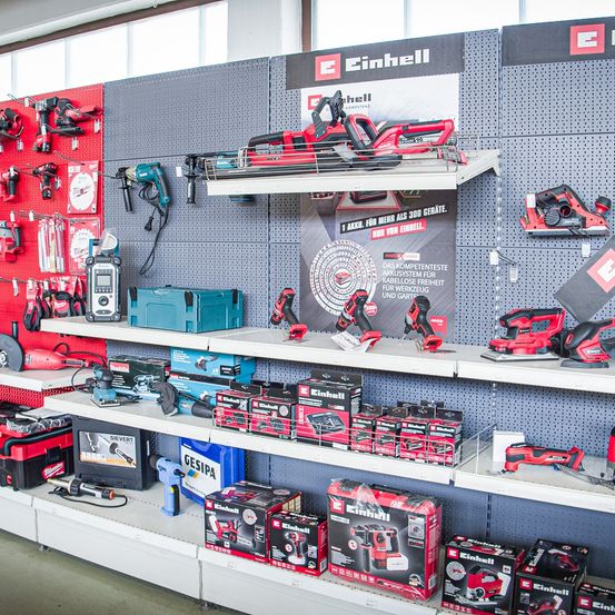 Ein Werkzeugladen zeigt verschiedene Einhell-Elektrowerkzeuge auf Regalen und Lochwänden. Modelle umfassen Bohrer, Sägen und kabellose Werkzeuge. Ein Banner mit dem Einhell-Logo ist ebenfalls ausgestellt.