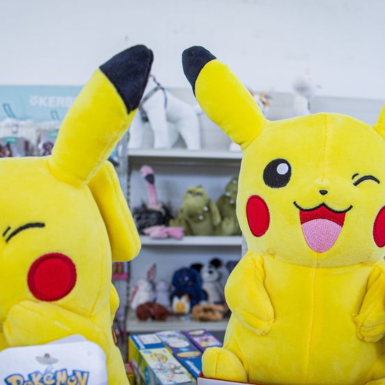 Zwei gelbe Pikachu-Plüschtiere sind in einem Geschäft ausgestellt, mit Regalen voller Spielzeug im Hintergrund.