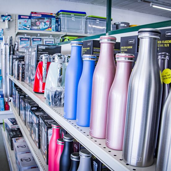 Ein Ladenregal gefüllt mit verschiedenen Edelstahlflaschen, einschließlich blauer, rosa und silberner Flaschen, die in einer Reihe ausgestellt sind.