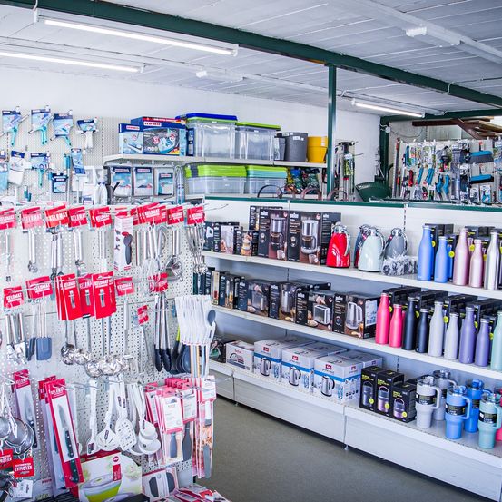 Ein Geschäft gefüllt mit verschiedenen Küchenartikeln wie Utensilien, Wasserkochern und Aufbewahrungsboxen, die an Regalen und Haken ausgestellt sind. Die Produkte reichen von Küchenwerkzeugen bis hin zu Getränkebehältern.
