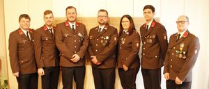 Eine Gruppe von Personen in formellen Militäruniformen steht in einer Reihe, lächelt und hat Medaillen auf der Brust, vor einer hellen Wand.