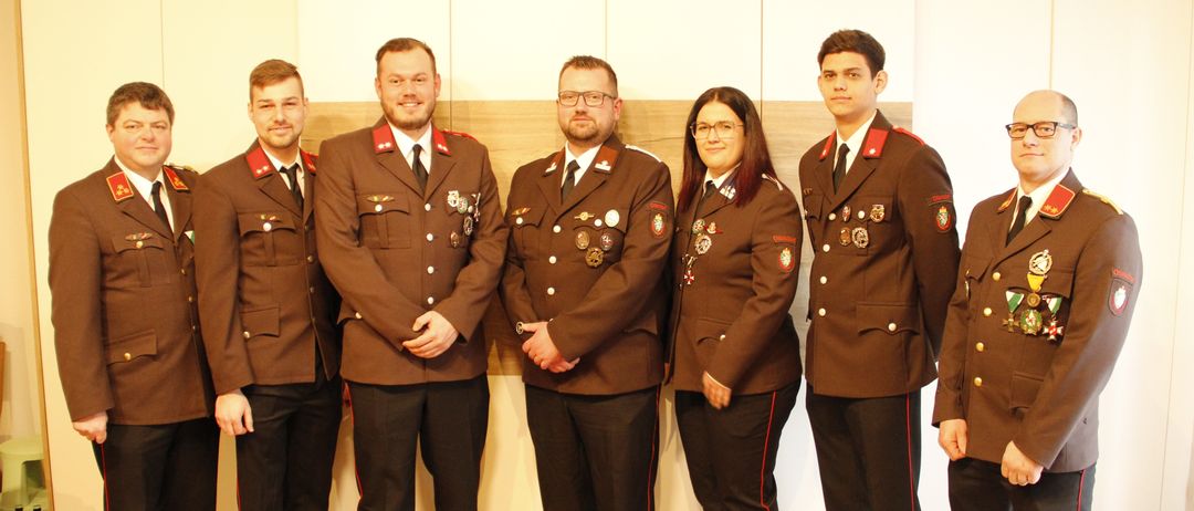 Eine Gruppe von Personen in formellen Militäruniformen steht in einer Reihe, lächelt und hat Medaillen auf der Brust, vor einer hellen Wand.