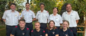 Eine Gruppe von Feuerwehrleuten in Uniform posiert für ein Foto in einem Park mit Bäumen im Hintergrund.