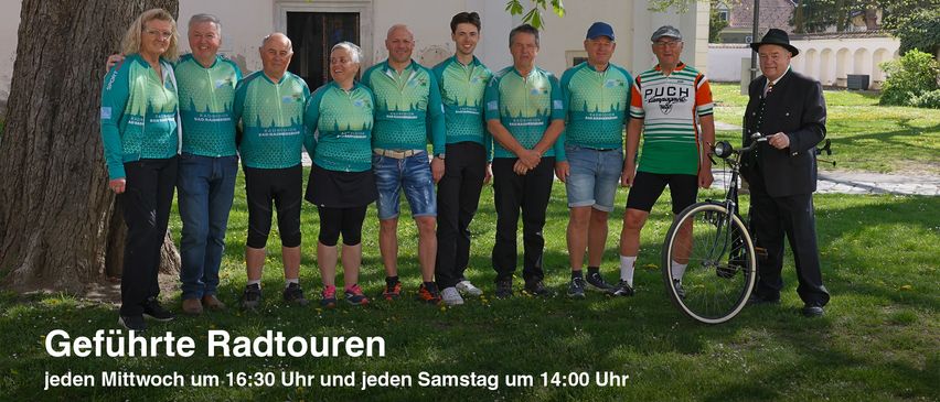 Sieben Radfahrer stehen vor einem Gebäude mit einem Baum. Sie tragen Radtrikots und Turnschuhe. Ein Fahrrad ist auf der rechten Seite geparkt. Der Text 'Radtouren' ist in der unteren linken Ecke gedruckt. Die Zeit ist unter dem Text angegeben. Das Bild hat einen Wasserzeichen auf der unteren rechten Ecke.