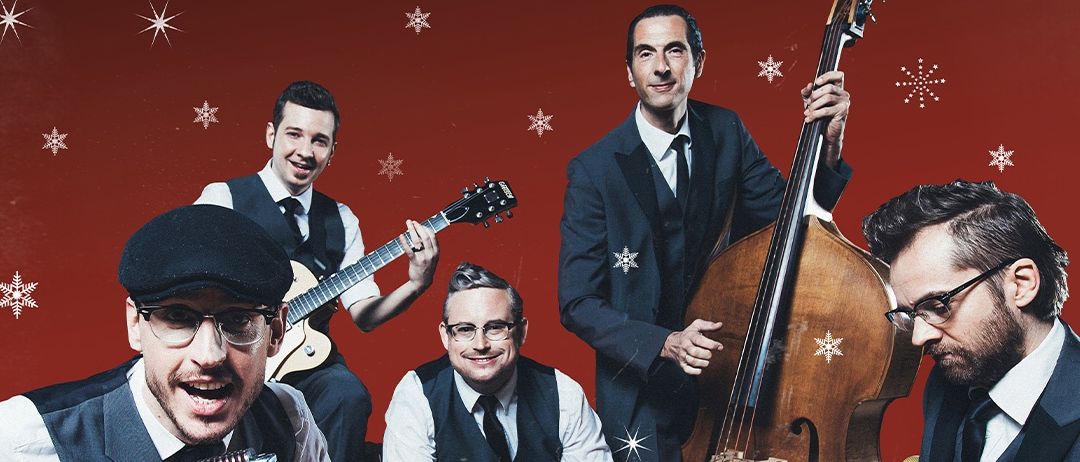 Eine Band von fünf Männern, die Anzüge, Hüte und Brillen tragen, posiert für ein Foto in einem mit Weihnachtssternen dekorierten Raum. Jeder Mann spielt ein Musikinstrument.