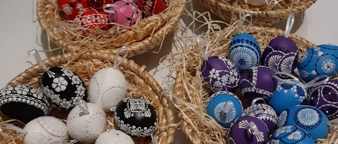 Vier Körbe zeigen dekorative Eier. Ein Korb hat rote Eier mit weißen Blumendesigns. Ein anderer hat weiße Eier mit schwarzen Mustern. Der dritte Korb enthält blaue Eier mit weißen Blumendesigns. Der letzte Korb hält lila Eier mit weißen Mustern.