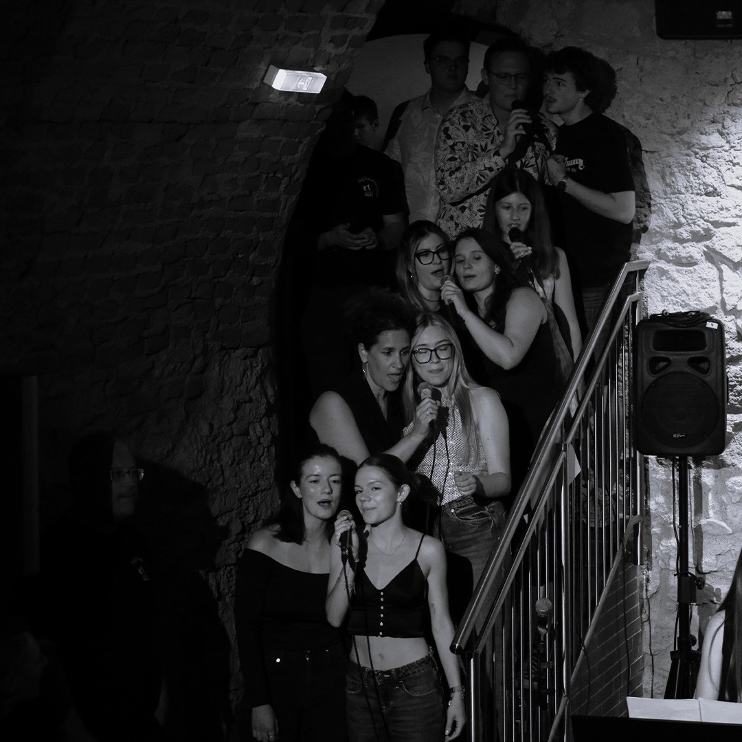 Gruppe von Menschen singt bei einem Karaoke-Event auf einer Treppe in einem Steinbunker.