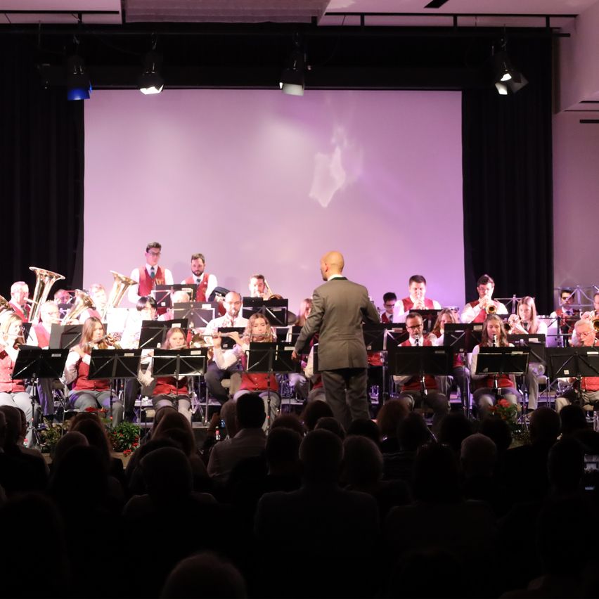 Eine Band spielt auf der Bühne mit Musikinstrumenten unter Bühnenlichtern vor einem Publikum.