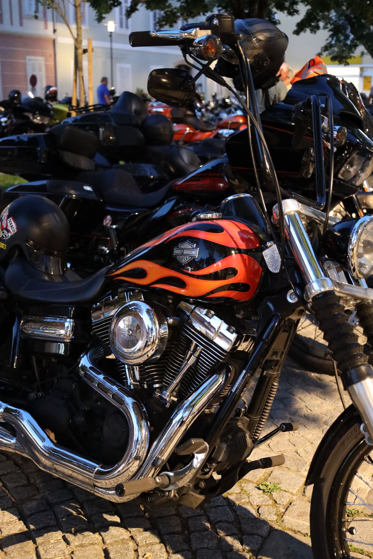 Nahaufnahme eines Harley-Davidson-Motorrads mit schwarzem und rotem Flammendesign auf dem Tank, geparkt zwischen anderen Motorrädern.