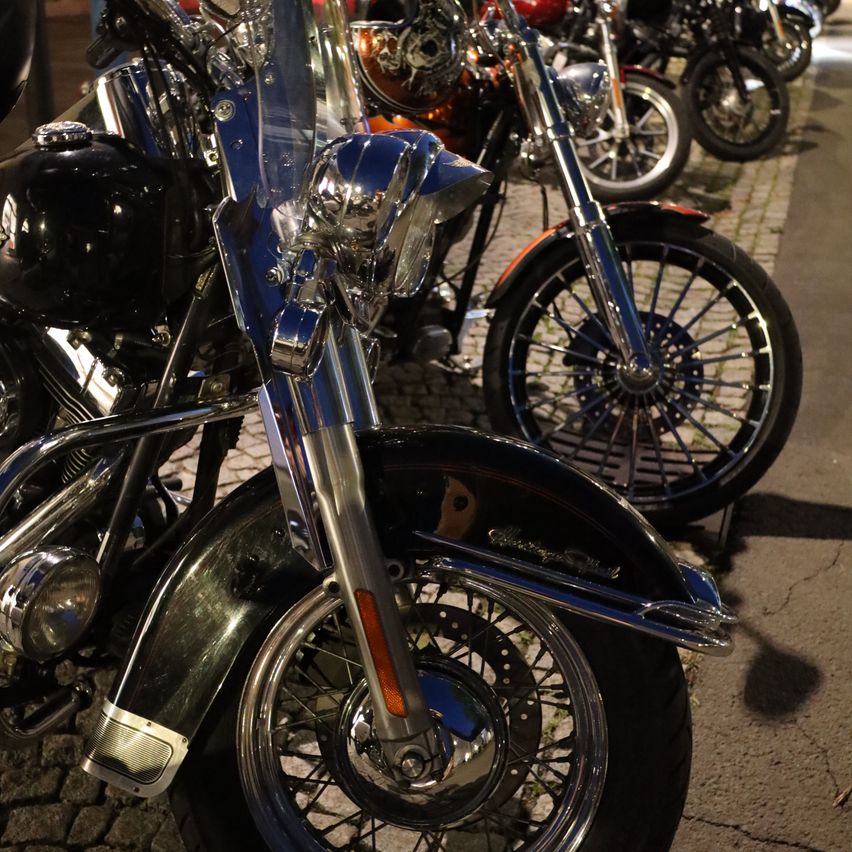 Eine Nahaufnahme eines glänzenden schwarzen Motorrads mit Chrom-Details, das nachts auf einer Kopfsteinpflasterstraße geparkt ist.