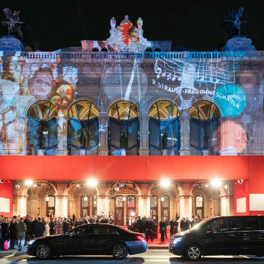 Ein großes Gebäude mit einem roten Vordach und einer blauen Lichtshow auf der Fassade, mit Menschen, die sich draußen versammeln.