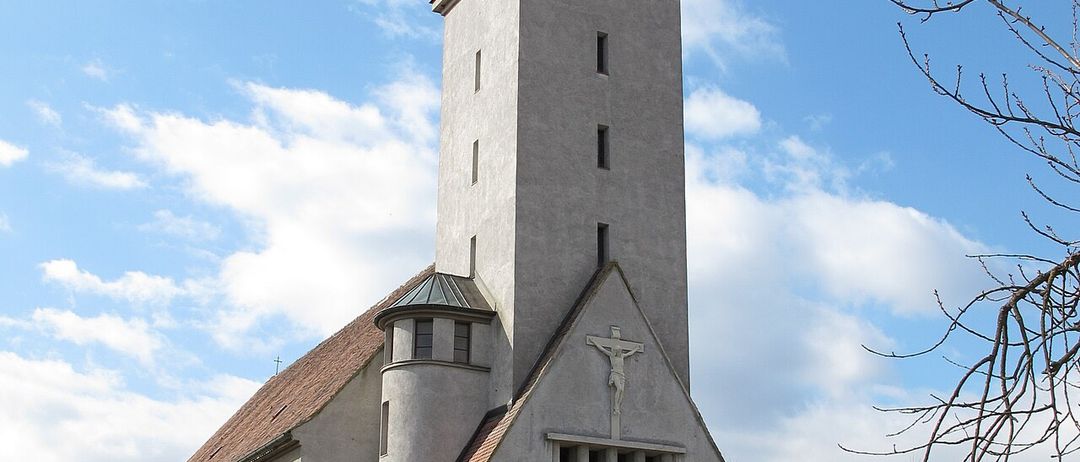 Eine Kirche mit einem Turm, einem braunen Dach und einer Statue von Jesus an der Fassade. Zwei Statuen flankieren den Eingang.