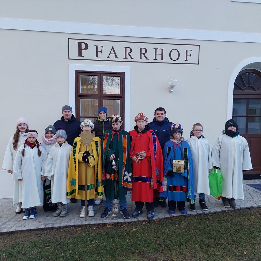 Eine Gruppe von Menschen in traditionellen Kostümen posiert für ein Foto vor einem Gebäude namens Pfarrhof.