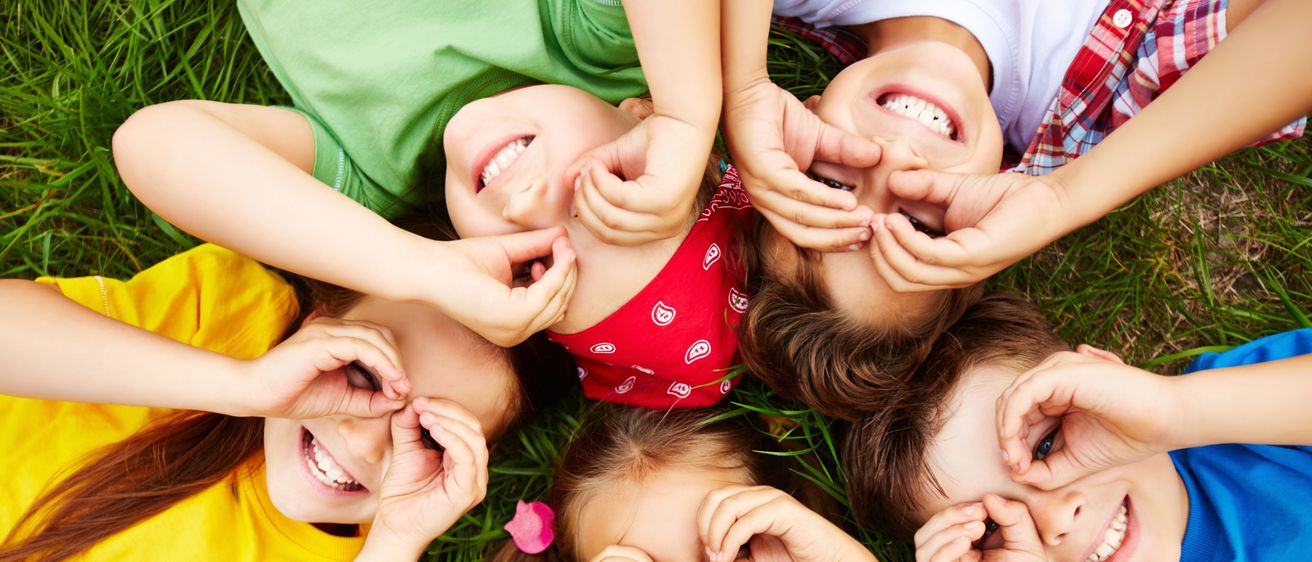 Gruppe von Kindern liegt auf einem Rasen, sie lächeln und bilden einen Kreis mit ihren Händen.