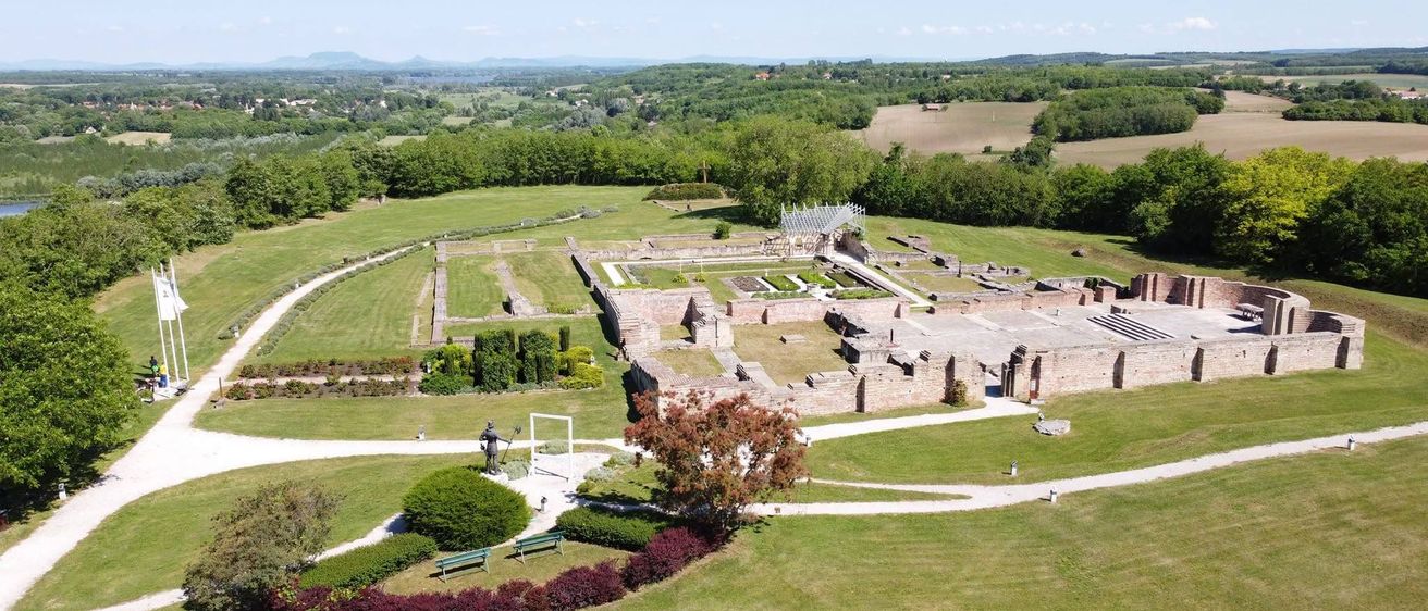 Luftaufnahme einer antiken römischen Villa mit einer Statue, umgeben von üppigem Grün und einem klaren Blick auf die umliegende Landschaft.