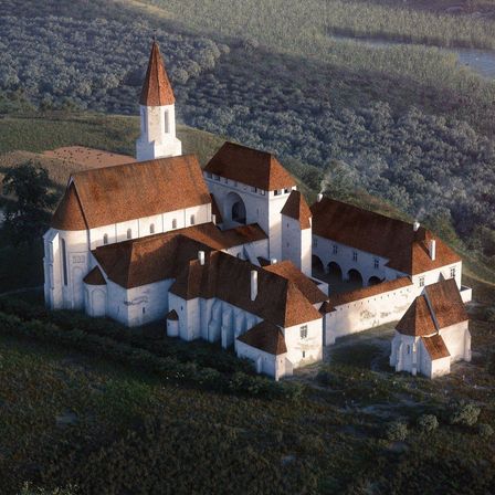 Eine Luftaufnahme einer mittelalterlichen Burg mit einem hohen Turm und mehreren Gebäuden mit braunen Dächern. Die Burg ist von üppigem Grün und einem Gewässer umgeben.
