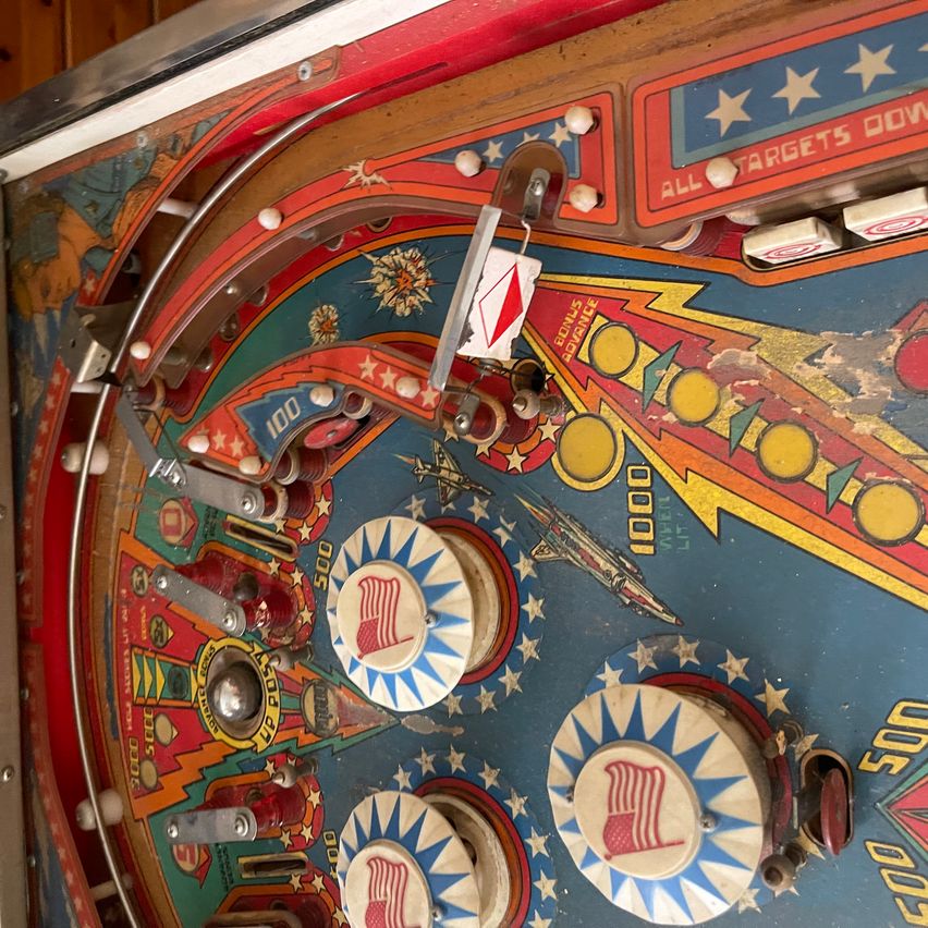 Close up of an old pinball machine with a red, white, and blue design and numbers 500, 1000, and 2000.