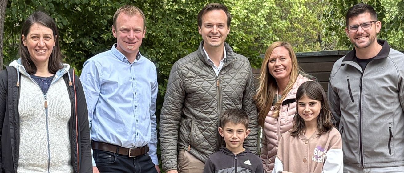 Eine Gruppe von Menschen, darunter zwei Kinder, steht auf einer Holzplattform im Freien und posiert für ein Foto. Sie halten ein Zertifikat in der Hand.