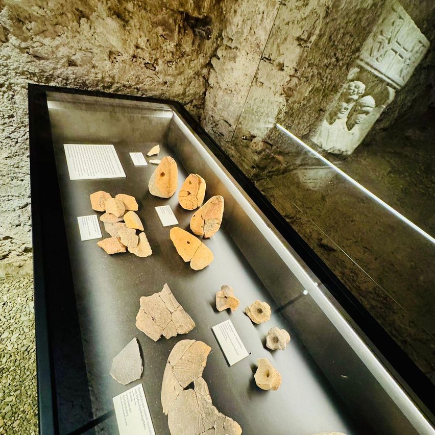 A display case in a museum holds ancient artifacts, including pottery fragments and wooden pieces, with informational labels.