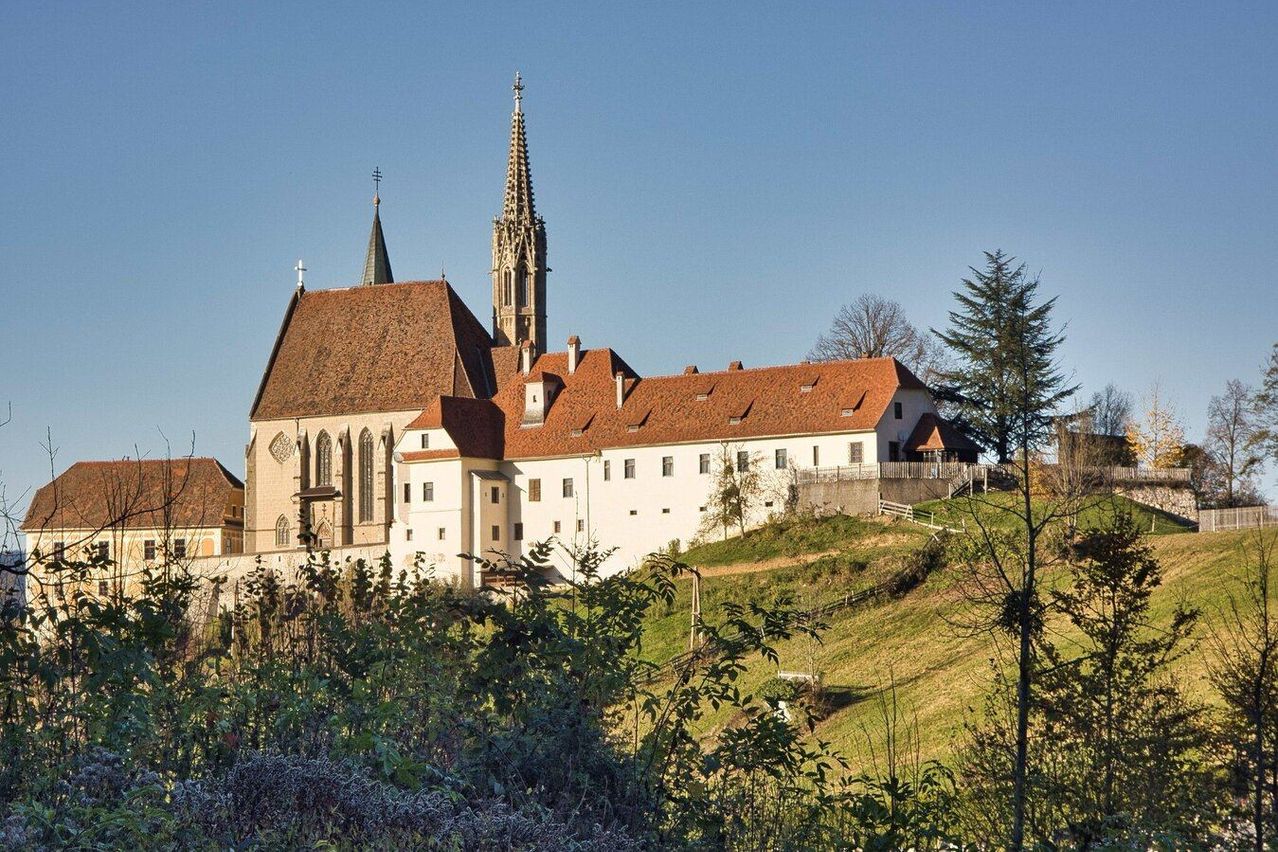 Eine große Kirche mit roten Dächern und einem hohen Turm steht auf einem Hügel unter einem klaren blauen Himmel.