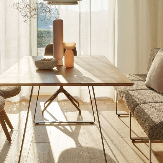 Ein modernes Esszimmer mit einem Holztisch und Stühlen. Ein beiger Sofa mit Kissen steht in der Nähe. Der Raum hat einen minimalistischen Stil mit klaren Linien und neutralen Farben.