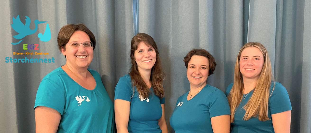 Vier Frauen in türkisfarbenen T-Shirts und Jeans stehen lächelnd vor einem grauen Vorhang und posieren für ein Foto.