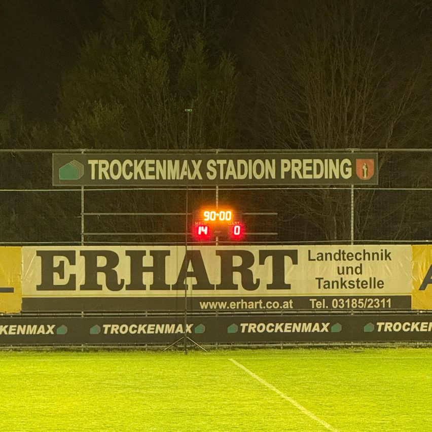 A soccer field with a scoreboard reading 90:00 and 14:0. Advertisement banners for Erhart Landtechnik und Tankstelle.