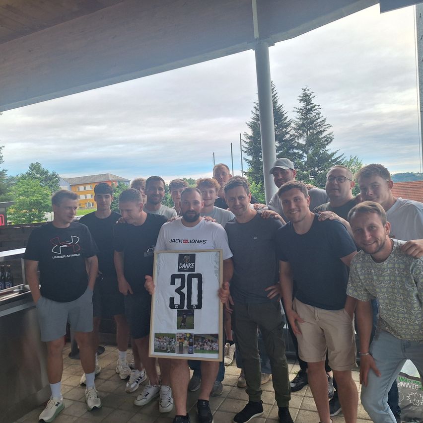 A group of men pose for a picture in a park. One man holds a framed number 30 jersey.