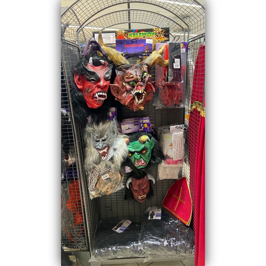 Ein Halloween-Laden mit verschiedenen Masken und Kostümen, darunter eine rote Teufelsmaske, eine gehörnte Teufelsmaske, eine Wolfsmaske und eine grüne Monstermaske.
