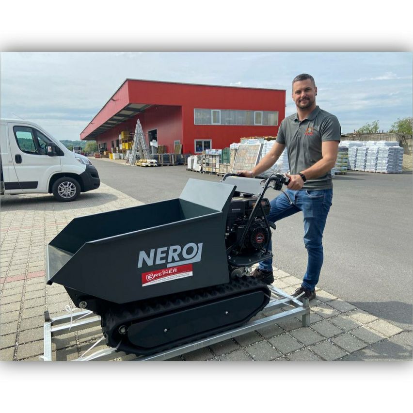 Ein Mann steht neben einem Raupenlader der Marke Nero vor einem großen roten Gebäude.