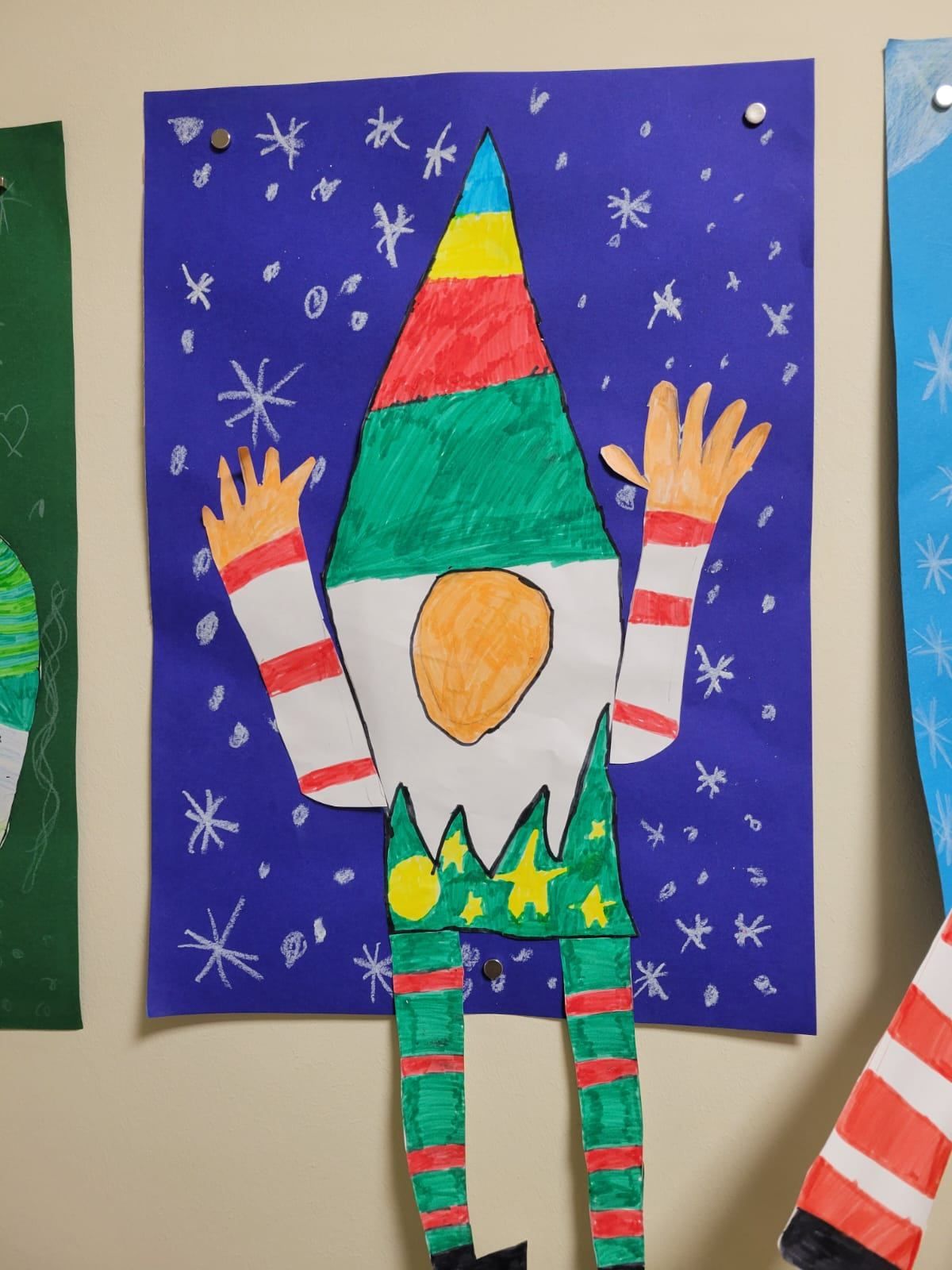 A vibrant hand-drawn paper gnome stands against a blue backdrop with snowflakes. It wears a multicolored conical hat and has outstretched arms.