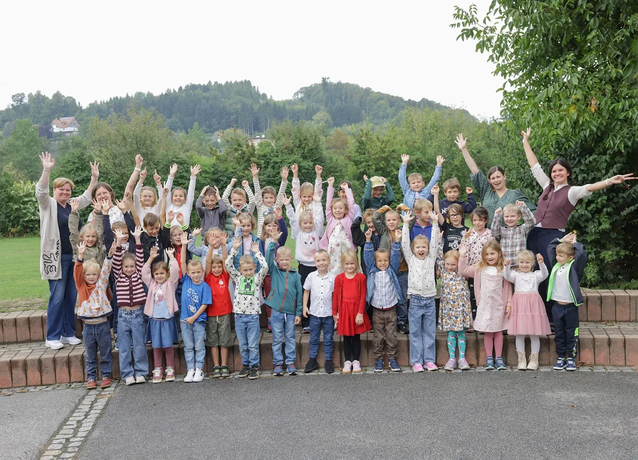 Eine große Gruppe von Kindern und Erwachsenen posiert für ein Foto im Freien mit einem Berg im Hintergrund.
